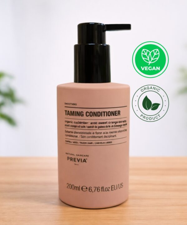 Frasco de Previa Taming Condicionador em tom rosa pastel com doseador preto, sobre uma base de madeira. O rótulo indica ser um condicionador disciplinante de 200ml para cabelos lisos, formulado com extratos orgânicos de amêndoa e sementes de linho. Ideal como condicionador pós alisamento, ajuda a controlar o frizz. No canto superior direito, destacam-se os selos "Vegan" e "Organic Product", reforçando a identidade natural da Previa Italia.