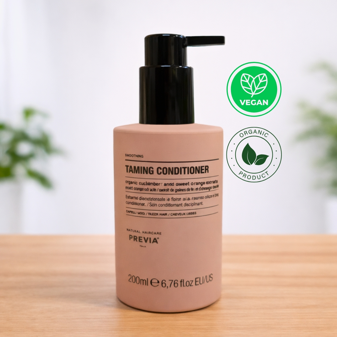 Frasco de Previa Taming Condicionador em tom rosa pastel com doseador preto, sobre uma base de madeira. O rótulo indica ser um condicionador disciplinante de 200ml para cabelos lisos, formulado com extratos orgânicos de amêndoa e sementes de linho. Ideal como condicionador pós alisamento, ajuda a controlar o frizz. No canto superior direito, destacam-se os selos "Vegan" e "Organic Product", reforçando a identidade natural da Previa Italia.