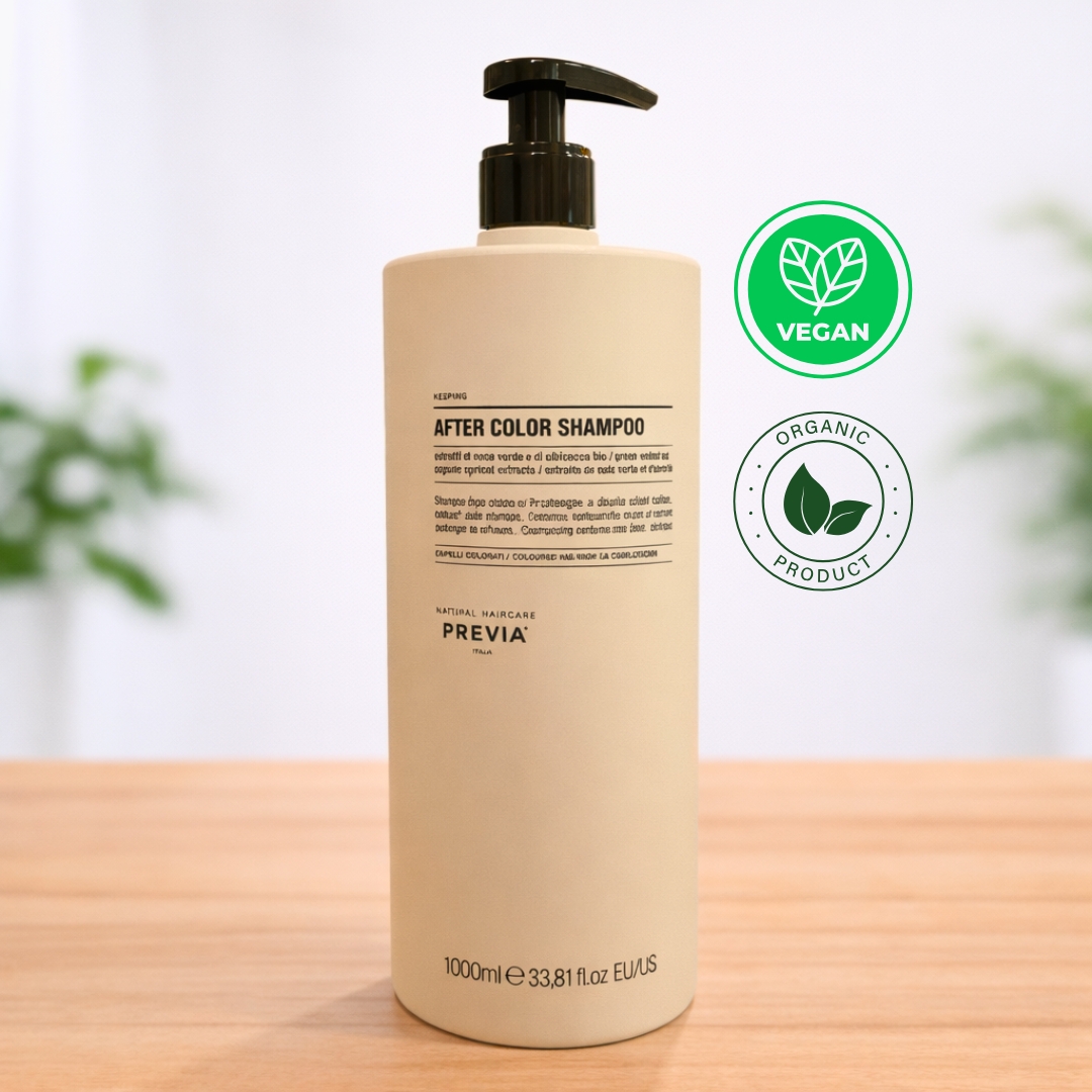 Frasco de Previa After Color Shampoo de 1000ml sobre uma superfície de madeira. Este shampoo pós coloração apresenta uma embalagem minimalista em tons de creme, formulada com extratos de noz verde e damasco orgânico para cuidar de cabelos pintados. No canto superior direito, destacam-se os selos "Vegan" e "Organic Product". O design elegante da Previa Italia reforça a qualidade profissional e o compromisso com ingredientes naturais.