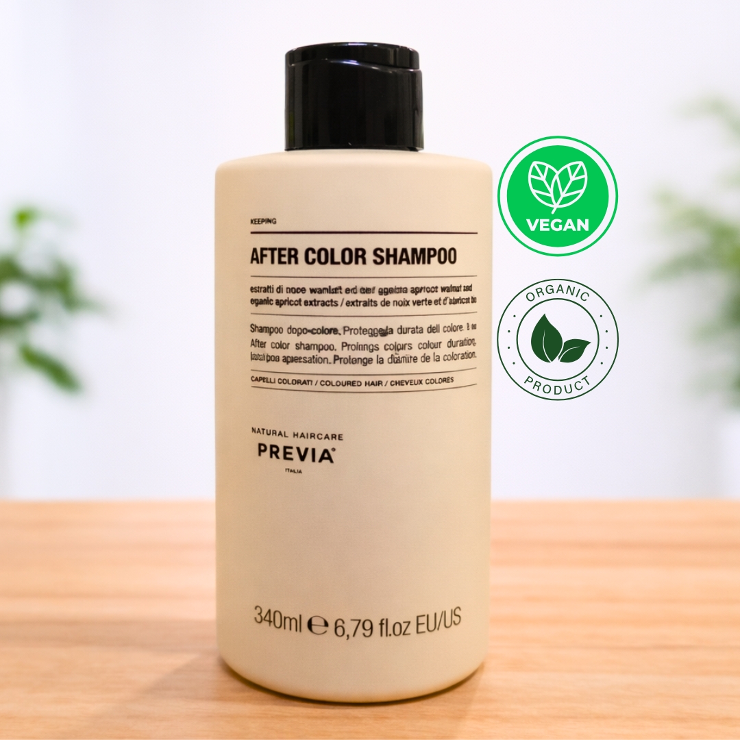 Frasco de Previa After Color Shampoo de 340ml sobre uma superfície de madeira. Este shampoo pós coloração apresenta uma embalagem minimalista em tons de creme, formulada com extratos de noz verde e damasco orgânico para cuidar de cabelos pintados. No canto superior direito, destacam-se os selos "Vegan" e "Organic Product". O design elegante da Previa Italia reforça a qualidade profissional e o compromisso com ingredientes naturais.